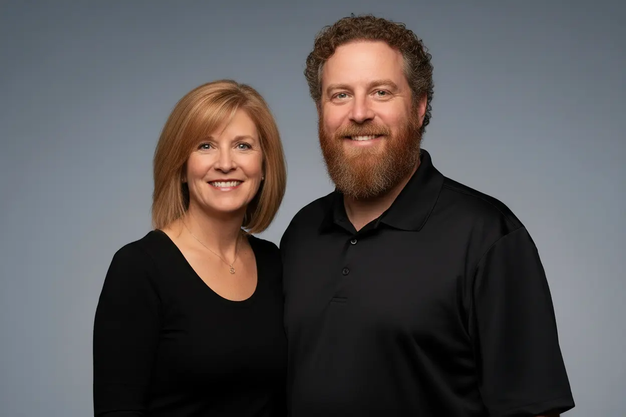 Sean and Maura Brodeur standing side by side in black work shirts against a plain gray backdrop, both smiling at the camera